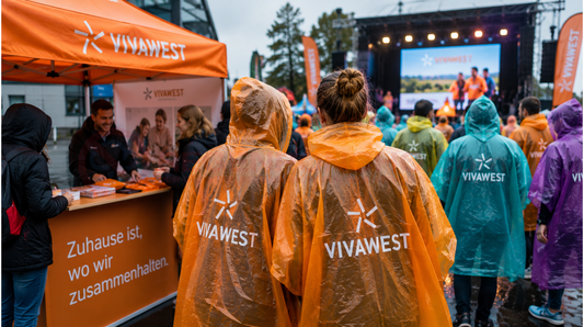 Besucher tragen bedruckte Regenponchos mit Firmenlogo bei einer Outdoor-Marketingveranstaltung im Regen.