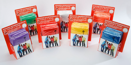Sieben Verkaufsdisplays mit Einweg-Regenponchos in einzelnen Farben – Lila, Grün, Rot, Gelb, Orange, Blau – jeweils mit roter Verpackung und Gruppenfoto auf der Vorderseite. Perfekt für Einzelhandel oder Eventverkauf.